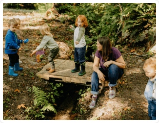 Molly with children on forest school bridge, one child pointing to water with surprised expression