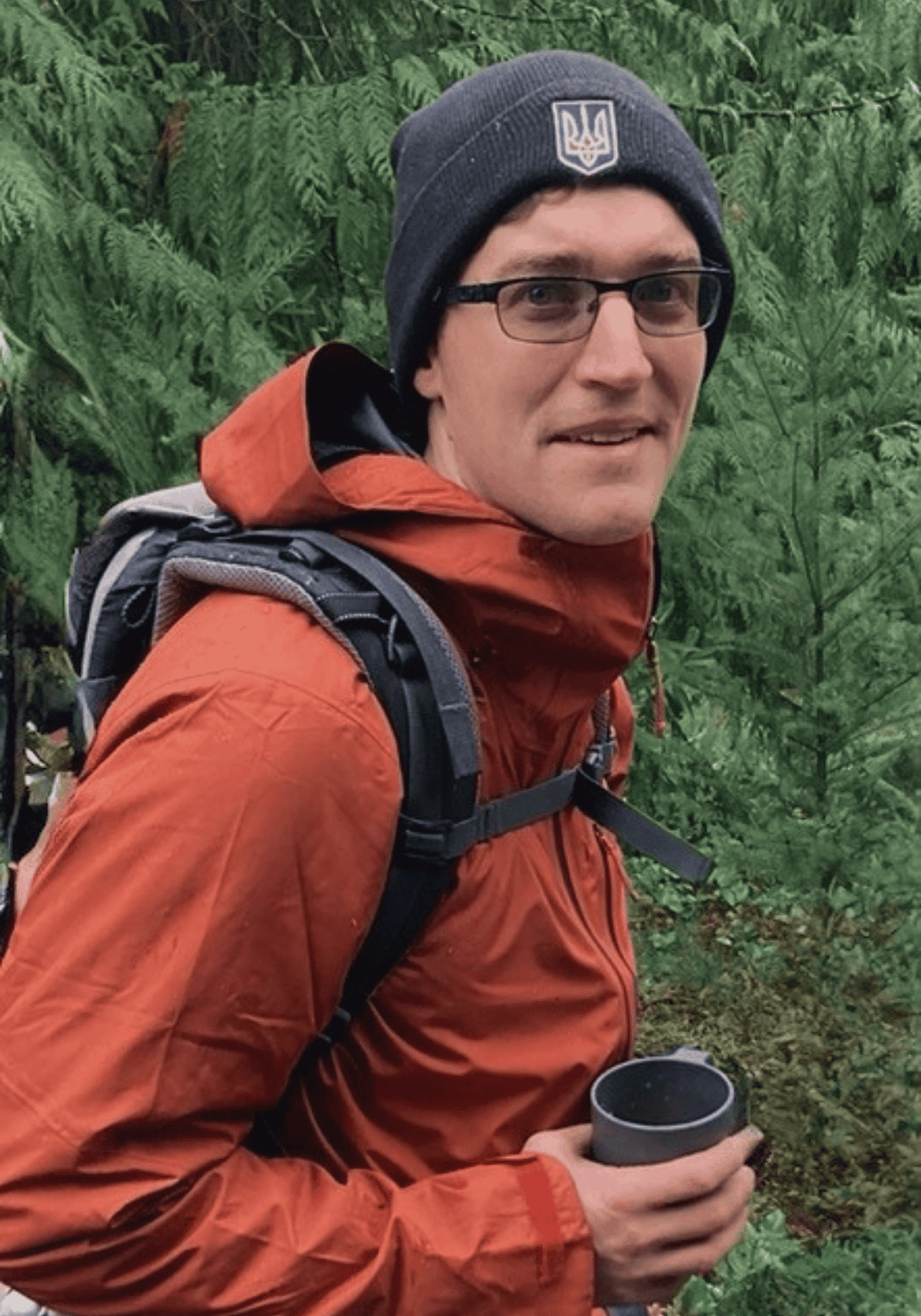 Jake Orear assistant director at Hidden Meadow forest school olympia washington portrait of him standing in front of forest holding a cup of coffee