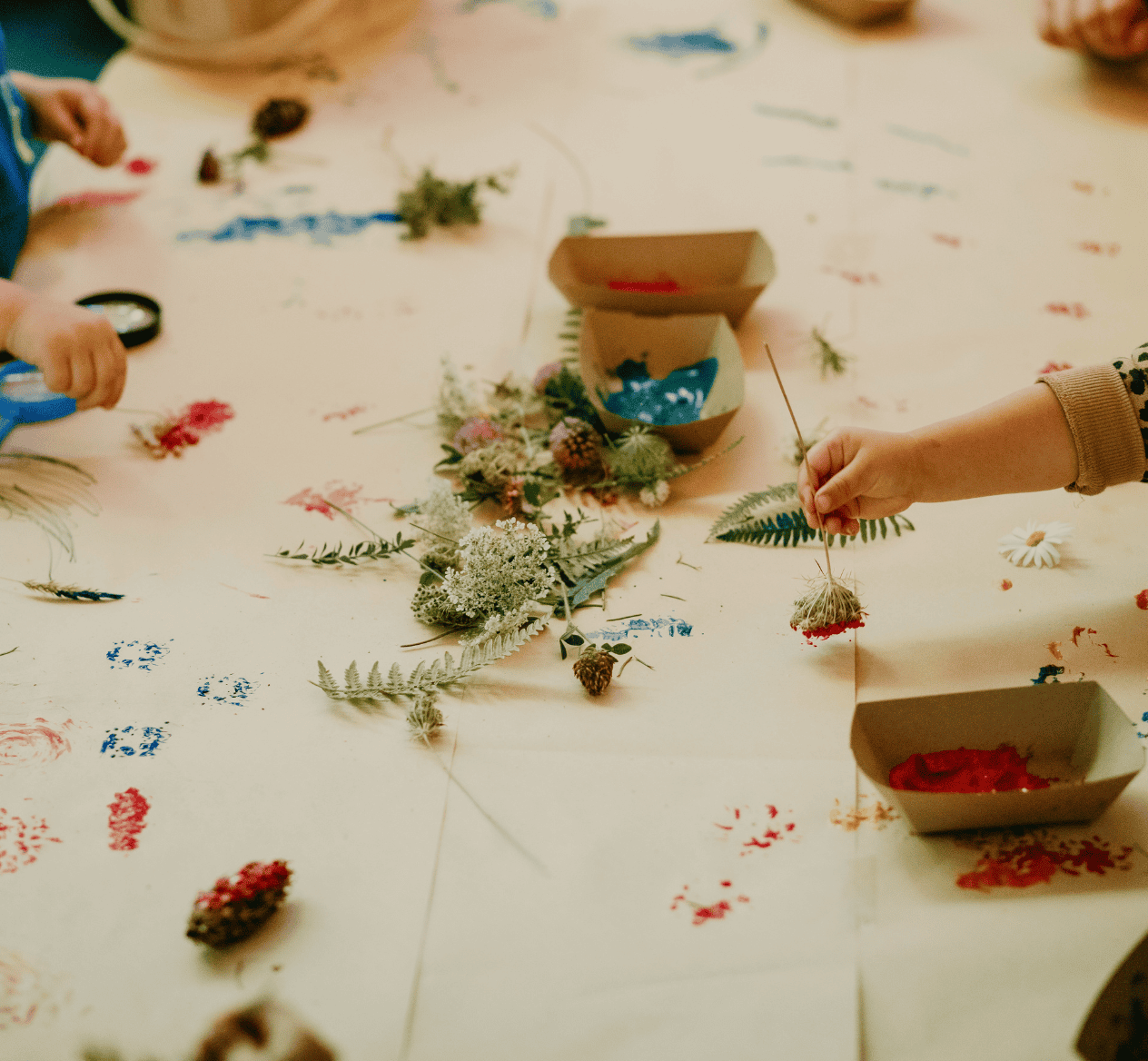 Children using flowers to paint on paper covered table at Hidden Meadow School showing creative play