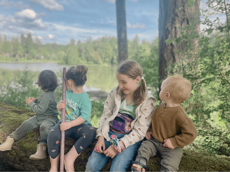 Children sitting on a log at Hidden Meadow School with Henderson Inlet behind them