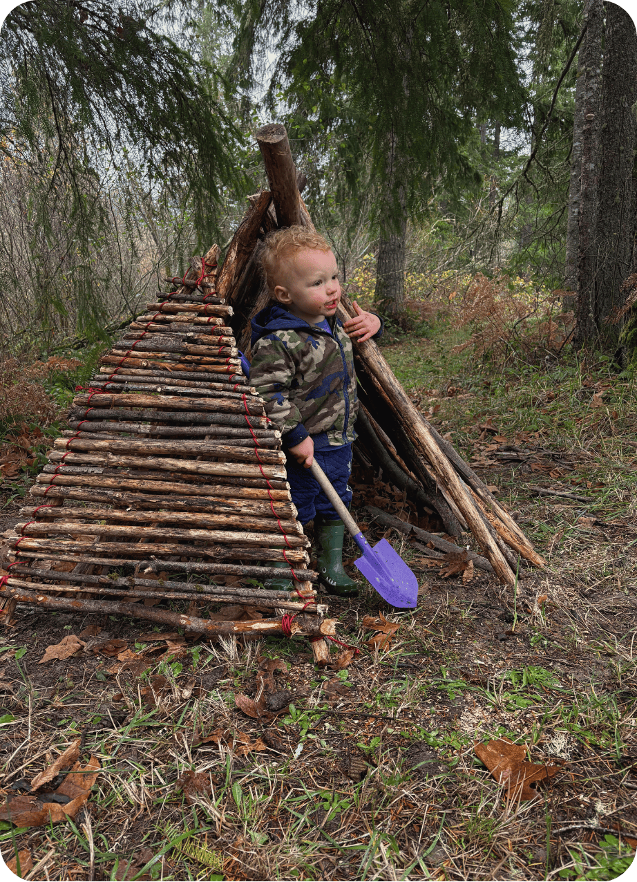 Child looking out of hand built fort made out of sticks at Hidden Meadow Outdoor school
