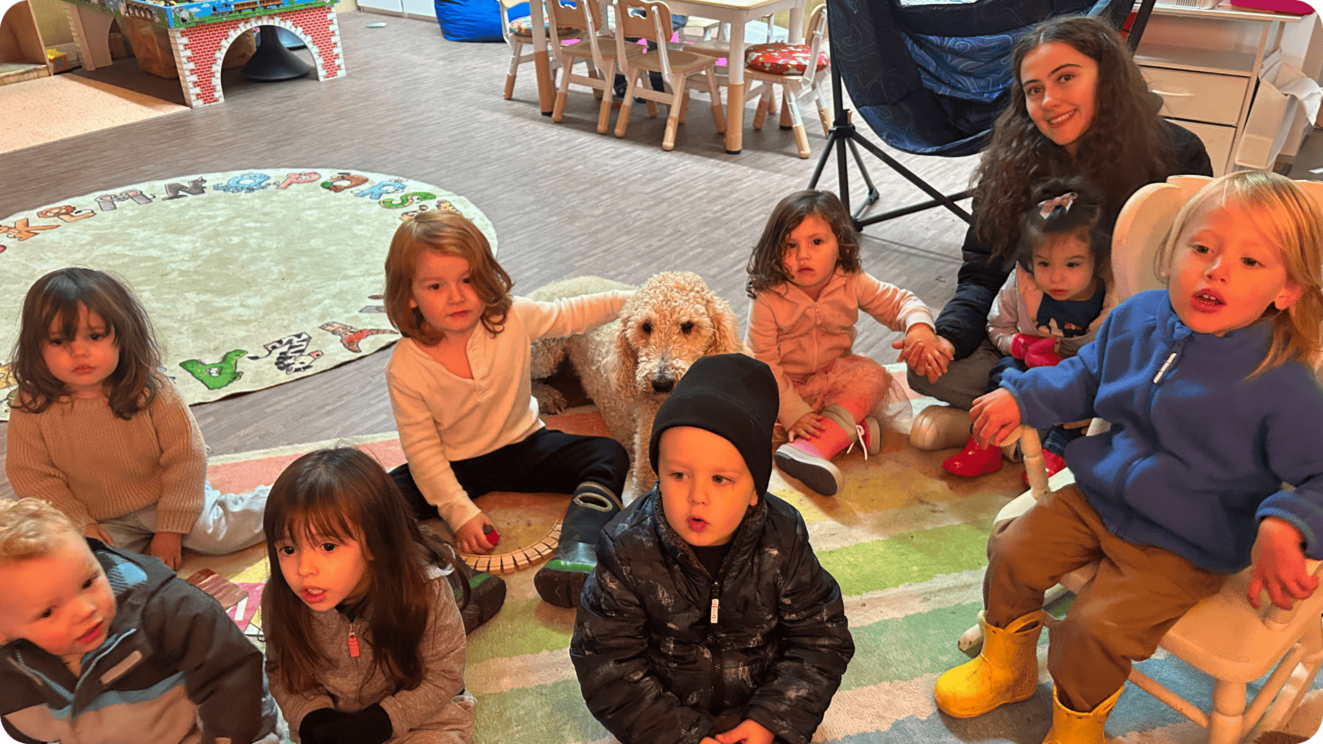 Child with arm around Wilma surrounded by children at Hidden Meadow School